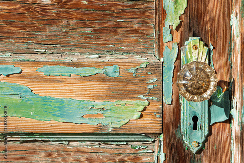 Φωτογραφία A close-up of peeling turquoise paint on an old wooden door with a vintage knob and backplate with a keyhole