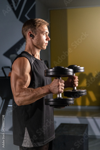 man is engaged in a workout executing hammer curls with dumbbells in a gym. He is focused on building arm strength while surrounded by fitness equipment.