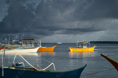 Tableau sur toile Bright yellow boats float on a tranquil sea beneath a moody, cloud-filled sky
