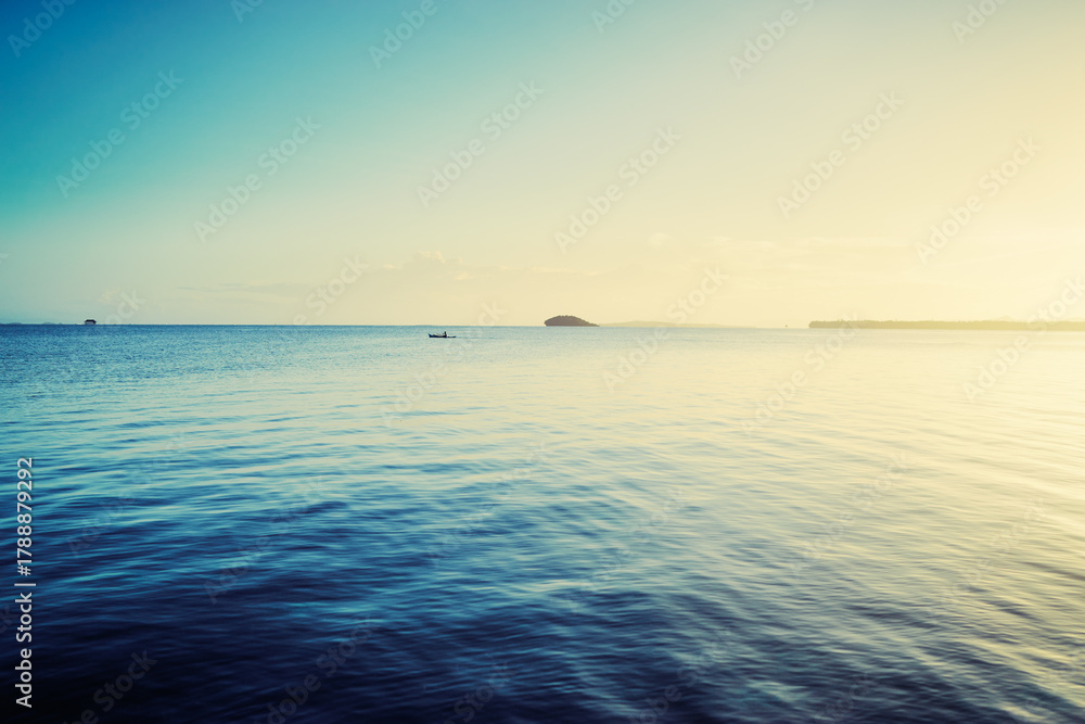 Obraz premium Peaceful Ocean Scene with Gentle Waves and a Distant Island at Sunrise