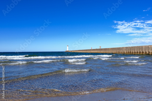 On the shore of Lake Ontario with small waves lapping the beach and the concrete pier at the Sodus Point Lighthouse
