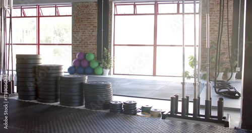 Occupying left-center foreground, stacks of bumper plates forming columns at studio gym with bars