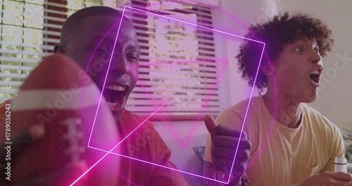 Fotografija Cheering friends in red and pale shirts on sofa at home, holding American footba