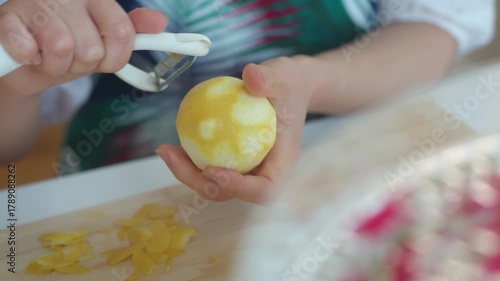Asian female hands peeling Lemon skin rind over a chopping board using a peeler, in a home kitchen setting.
