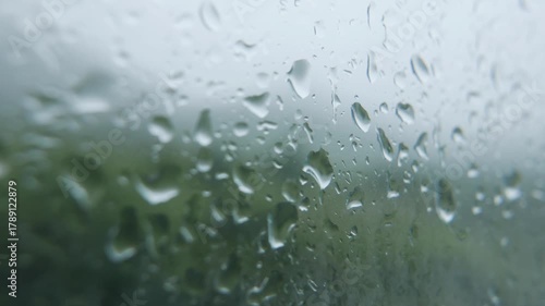 Macro shot of water droplets on window glass refracting daylight while gentle rain continues outside. Natural calm.