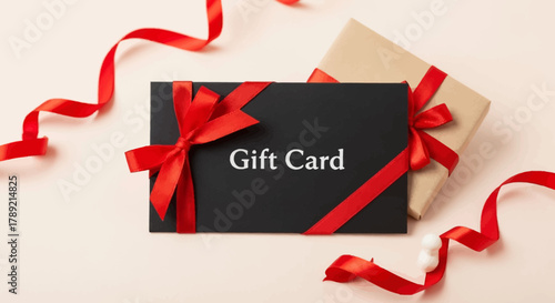 Gift Card Elegance: A stylish black gift card adorned with a vibrant red ribbon and a gift box beside it, on a muted-tone background, presents an atmosphere of elegance. 