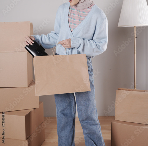Young woman's body in knitted sweater and jeans putting black leather purse into jumbo paper shopping bag