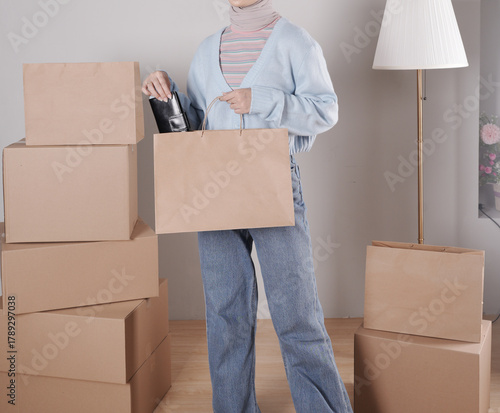 Young woman's body in knitted sweater and jeans putting black leather purse into jumbo paper shopping bag