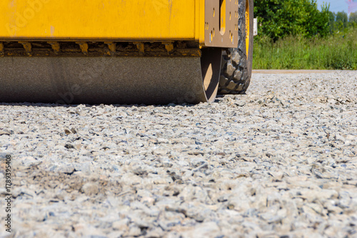 Close up of road roller steel drum compacting gravel layer for stable foundation under sunny outdoor conditions