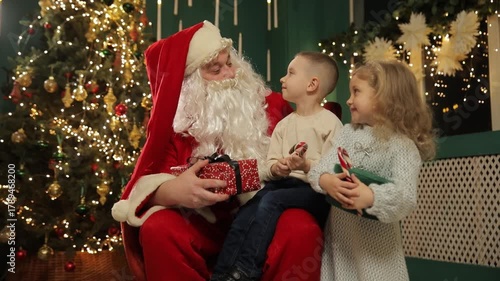 Children sitting with Santa near a decorated Christmas tree sharing holiday joy.