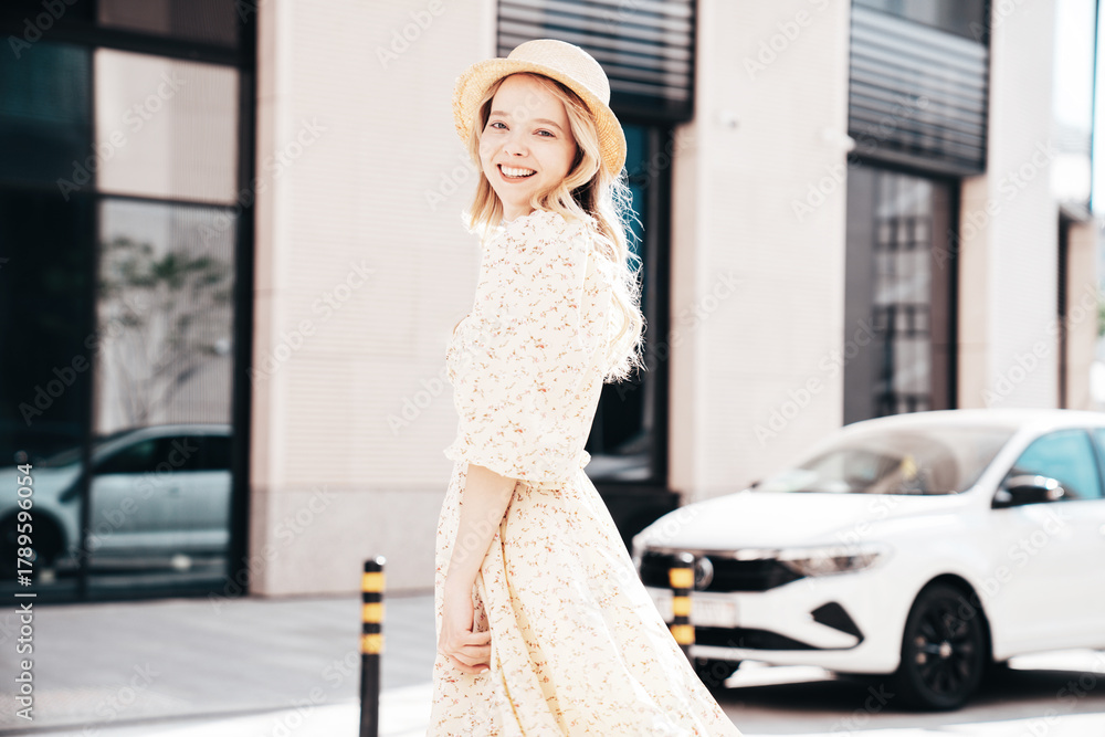 Naklejka premium Young beautiful smiling blond woman in trendy summer yellow dress. Sexy carefree woman posing in street at sunset. Positive model outdoors at sunny day. Cheerful and happy. In hat