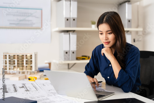 Young female engineer designer or contractor working on drawing plans analyzing structure on laptop computor at construction site office. copy space.