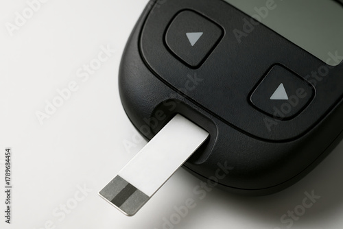 Macro view of a digital glucometer with a white test strip inserted, symbolizing blood sugar testing and precise medical monitoring for diabetes.