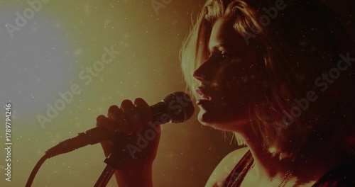 Singing female singer wearing dark sleeveless top holding wired mic on stage with mic stand, cable