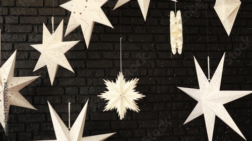 Hanging star lanterns lights during holiday winter season. Decoration White Christmas stars in black brick wall. A lamp in shape of star. Paper lightning lantern in star from. Star Xmas Paper Lantern