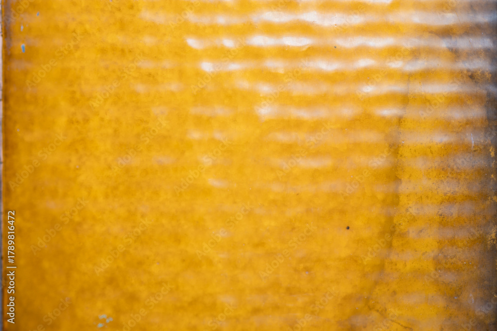 Fototapeta premium Bright yellow textured surface with wavy patterns caught in natural light during daytime