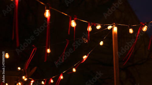 Warm string lights with red ribbons illuminate a dark outdoor space, creating a cozy, holiday festive mood perfect for a family or friends gathering under twinkling bulbs.