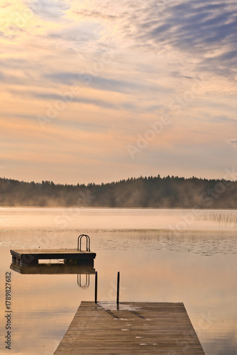 Jetty and floating island in the soft light of sunrise over a lake in Sweden.