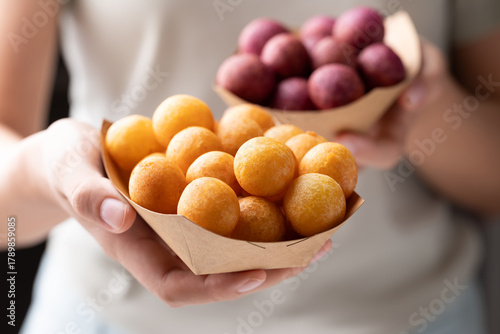 Deep fried sweet potato balls in paper bowl holding by hand, Thai street food snack