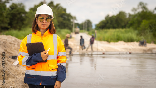 Foto A woman in a hard hat and safety jacket stands by a waterway, holding a clipboard