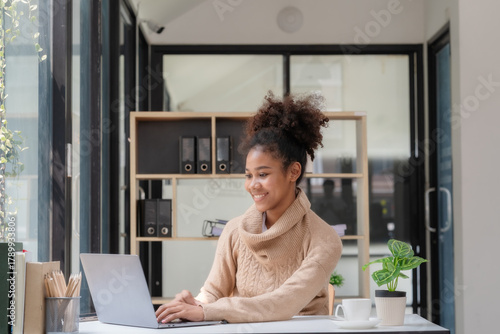 A happy professional businesswoman worker employee sitting at a desk working on a laptop in a corporate setting. A smiling female student using computer technology learning online, doing web research.
