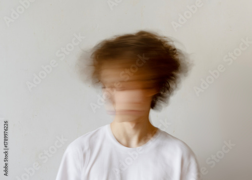 Blurred Face Of Young Person Shaking Head In White Shirt On Neutral Background. Concept Of Mental Health Struggles, Anxiety, Burnout Syndrome, Emotional Overload, And Psychological Disorder Awareness
