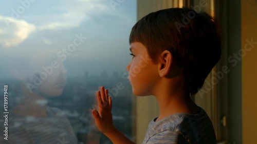 A young boy gazing thoughtfully out of a large window, reflecting on life and the cityscape at dusk