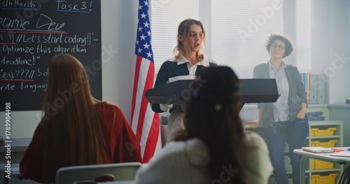 Schilderij op canvas American Female Student Delivers Speech With US Flag in Front of Classmates Sitting Desks