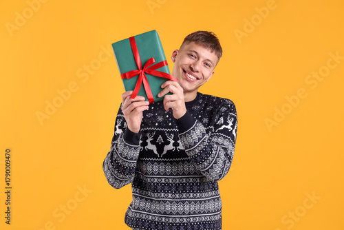 Smiling man in sweater with gift box on yellow background. Merry Christmas and Happy holidays
