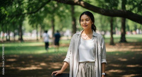 Southeast Asian woman with dewy natural skin and subtle makeup wearing light casual clothing, standing in an outdoor park under diffused daylight, captured in a relaxed natural pose and calm atmospher
