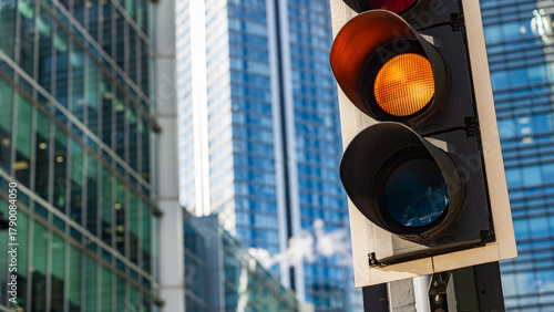 Amber traffic light glowing in front of modern glass office towers in financial district