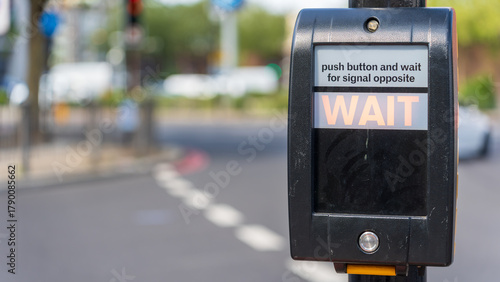 Pedestrian crossing wait button on black signal box beside city street intersection