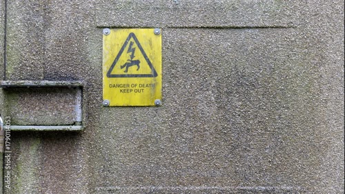 A yellow danger of death sign shot against a textured concrete wall.