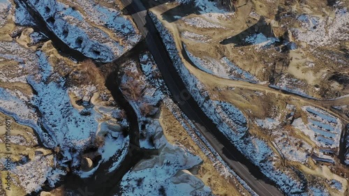 Aerial view of a winding road cutting through the snow dusted, rugged landscape of Cappadocia, the unique rock formations creating a stark contrast, Goreme, Cappadocia, Turkiye.