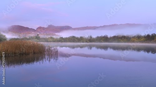 Misty Elterwater lake with peaceful reflections of mountains in The Lake District, UK.
