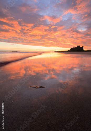 Colourful sunrise reflections on beach at Bamburgh Castle in Northumberland, North East England, UK.