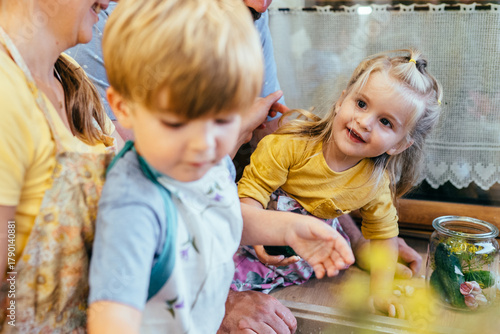 Close up of preschool children smiling and helping father with cucumbers in kitchen