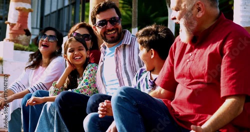 Indian family smiling on steps outdoors spending quality time together on green lawn, cheerful multi-generation portrait of grandparents, parents, and kids bonding, relaxing, enjoying leisure weekend