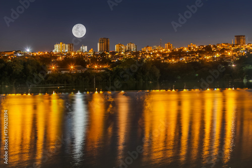 Full Moon Over City Skyline at Night with Water Reflections