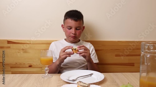 A boy eats and drinks juice while sitting at a table.