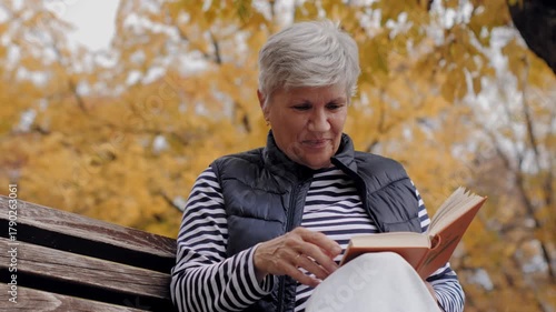 Senior woman reading a book and drinking coffee in autumn park