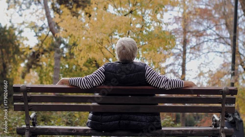 Elderly woman relaxing on a park bench in autumn