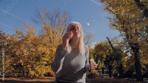 Happy blonde woman blowing soap bubbles in autumn park
