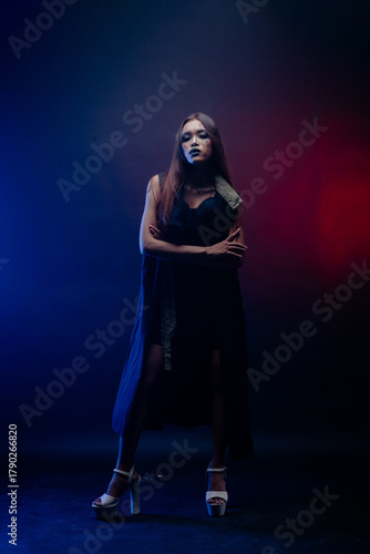 Fashion inspired Asian girl standing confidently under red and blue light, creating a bold studio aesthetic.