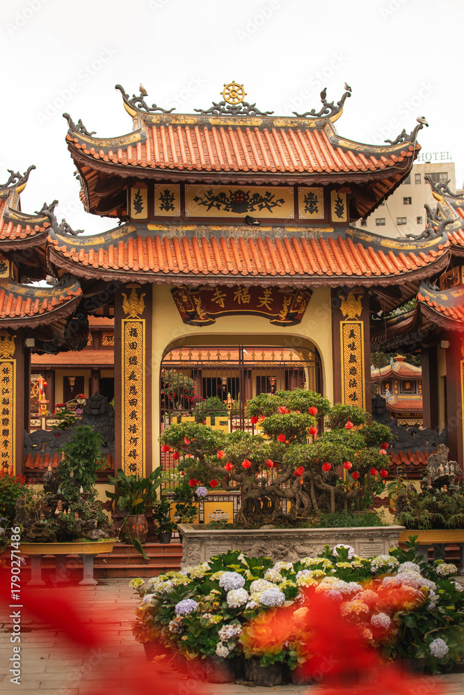 Obraz premium carved asian-style gate with roof at a buddhist temple, surrounded by plants, large bonsai, and hanging chinese lanterns