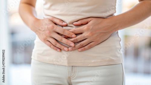 Wallpaper Mural Woman holding stomach in pain, experiencing discomfort and possible digestive issues, wearing light beige clothing in soft natural light Torontodigital.ca