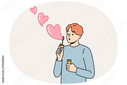 Romantic man uses heart-shaped soap bubbles to show love and kindness to people around him. Concept of romantic mood and desire to enter into serious relationship or marry girl you like