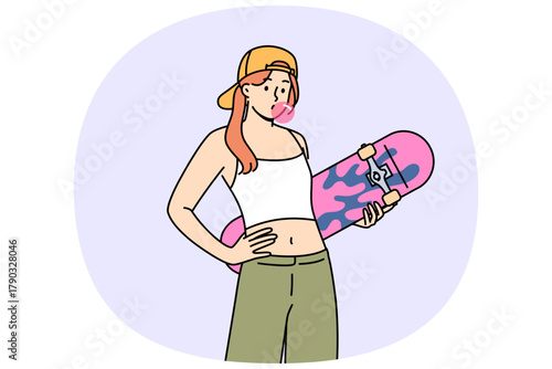 Teenage girl with skateboard in hands inflates bubble from chewing gum, demonstrating involvement in youth subculture. Gen z woman in crop top and wide-legged pants holds skateboard during summer walk