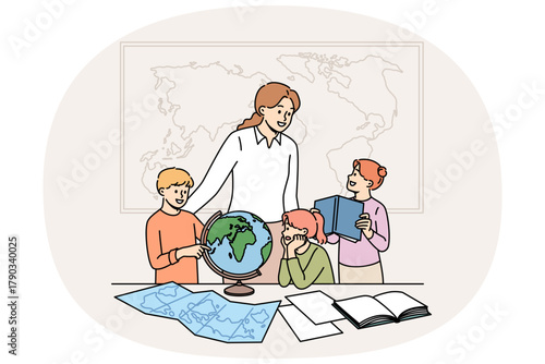 Geography teacher teaches small children using maps and globes or atlases, standing in classroom. Happy schoolchildren rejoice with interest learning new facts during geography lesson