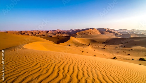 Fototapeta Naklejka Na Ścianę i Meble -  Vast desert landscape under a clear blue sky, featuring undulating sand dunes and distant mountain formations. The scene is bathed in warm sunlight